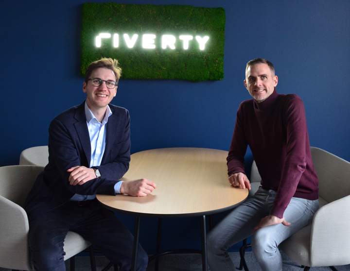 Vertreter von Riverty und Sinpex lächeln mit einem Riverty-Logo hinter sich