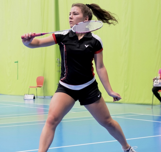 Thelma in an indoor badminton court, about to hit the shuttlecock.
