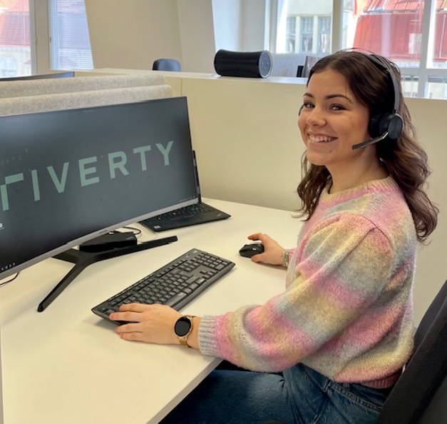 Thelma seated at her desk with 'Riverty' displayed on the computer screen.