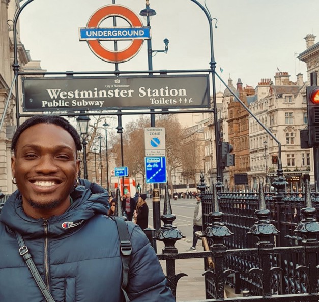 Timothy warmly dressed, standing in front of a 'Westminster Station' sign