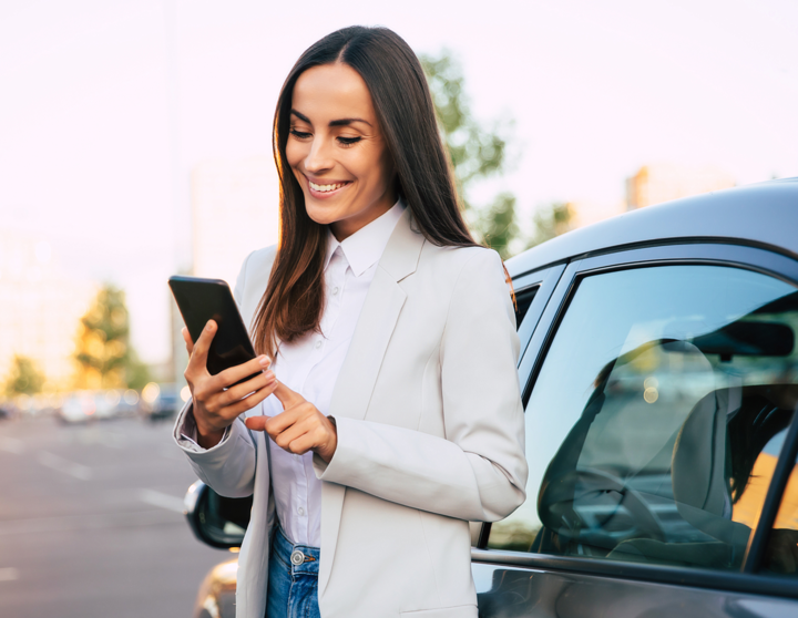 Woman standing at a parking lot next to car smiling down at her phone