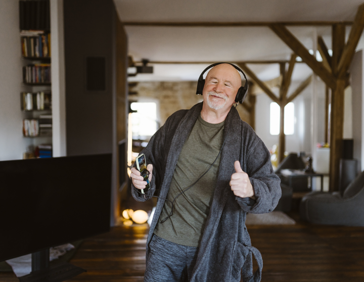 Een oudere man danst vrolijk in zijn appartement met een koptelefoon op