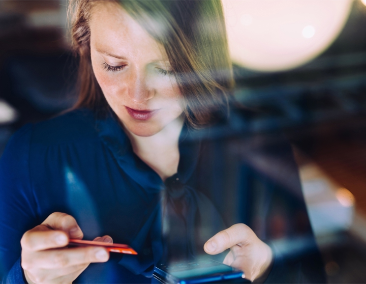 Jonge vrouw kijkt naar haar betaalpas terwijl ze online aan het shoppen is