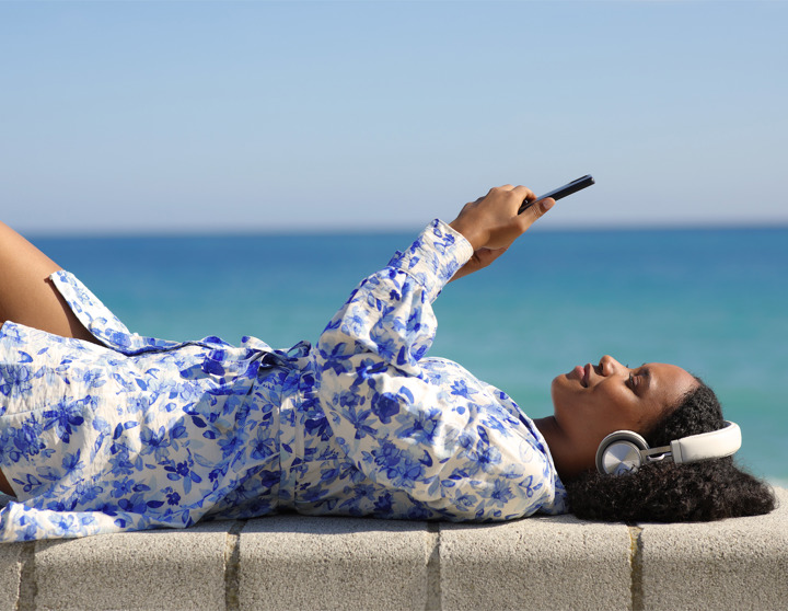 En vrouw ligt met een koptelefoon en een telefoon in haar hand