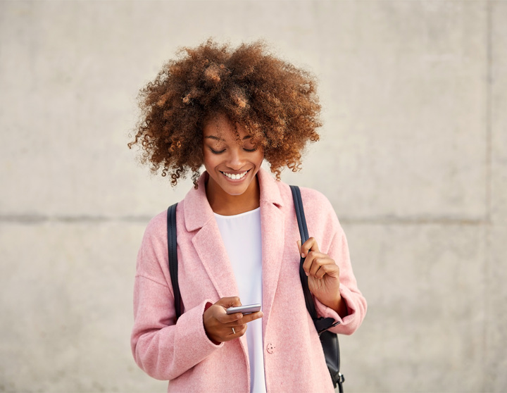 Een jonge vrouw in een roze shirt kijkt naar haar mobiele telefoon en glimlacht