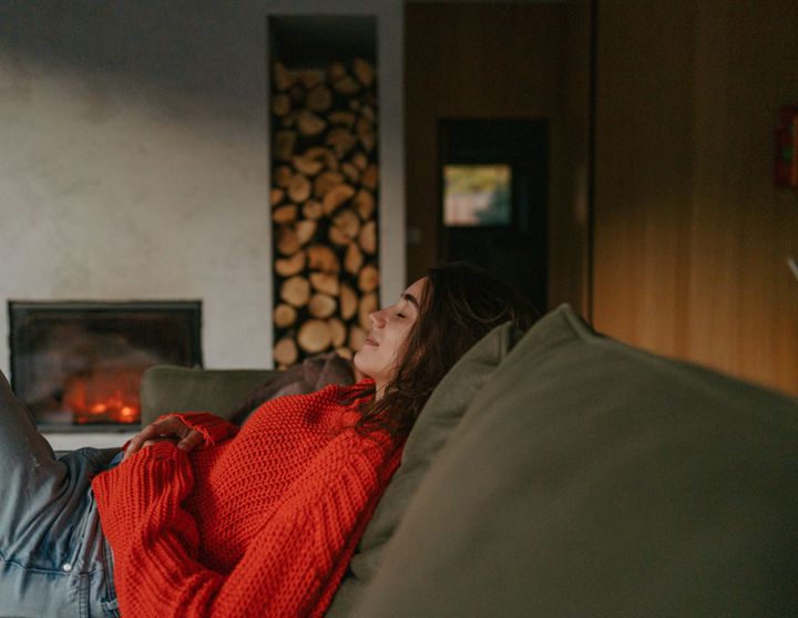 Een jonge vrouw zit comfortabel op haar bank met een kopje thee en kijkt uit het raam