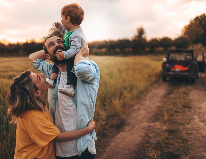 Eine junge Familie umarmt sich und steht an einem Feld. Sie haben sich mit einem geringen Budget ein Auto angeschaffen.