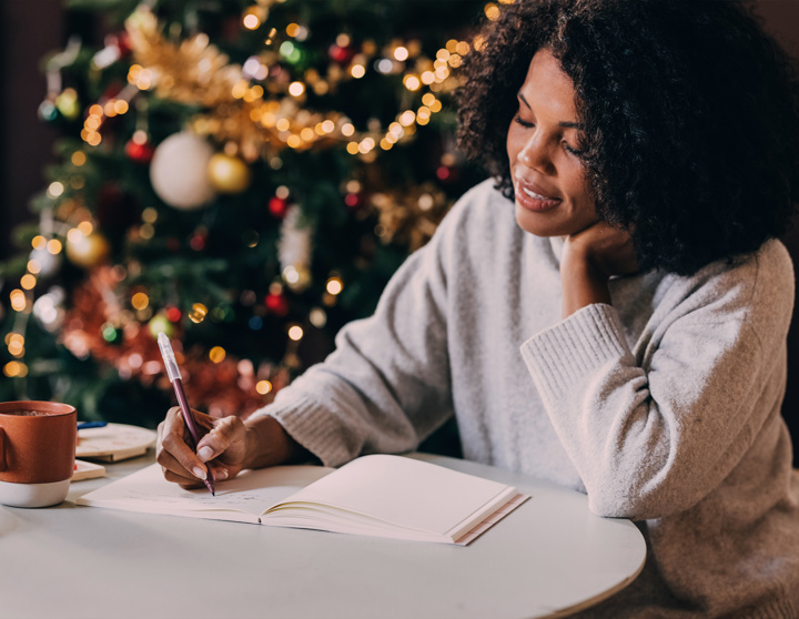 Een mevrouw zit in gezellige kerstsfeer en schrijft iets in een notitieboekje