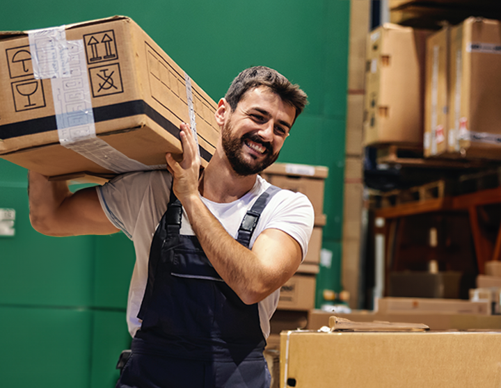 A warehouse worker lifts a box in a stocked warehouse.